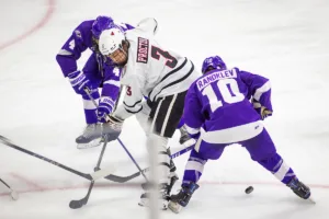 Omaha Mavericks defenseman Kirby Proctor (3) fights for the puck against Niagara Purple Eagles forward Carter Randklev (10) and forward Glebs Prohorenkovs (4) in the third period during a college hockey match on Friday, October 13, 2023, in Omaha, Nebraska. Photo by John S. Peterson.