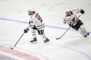 Omaha Mavericks forward Ty Mueller (19) moves the puck down the ice with forward Jacob Guevin (10) in the third period against the Niagara Purple Eagles during a college hockey match on Friday, October 13, 2023, in Omaha, Nebraska. Photo by John S. Peterson.