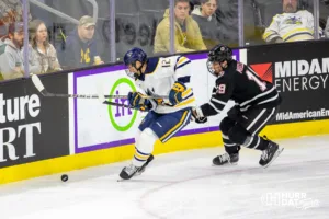 Augustana Viking forward Hunter Bischoff (12) and Omaha Maverick forward Ty Mueller (19) fight to get to the puck in the second period during the hockey match on Saturday, November 25, 2023, in Sioux Falls, SD. Photo by John S. Peterson.